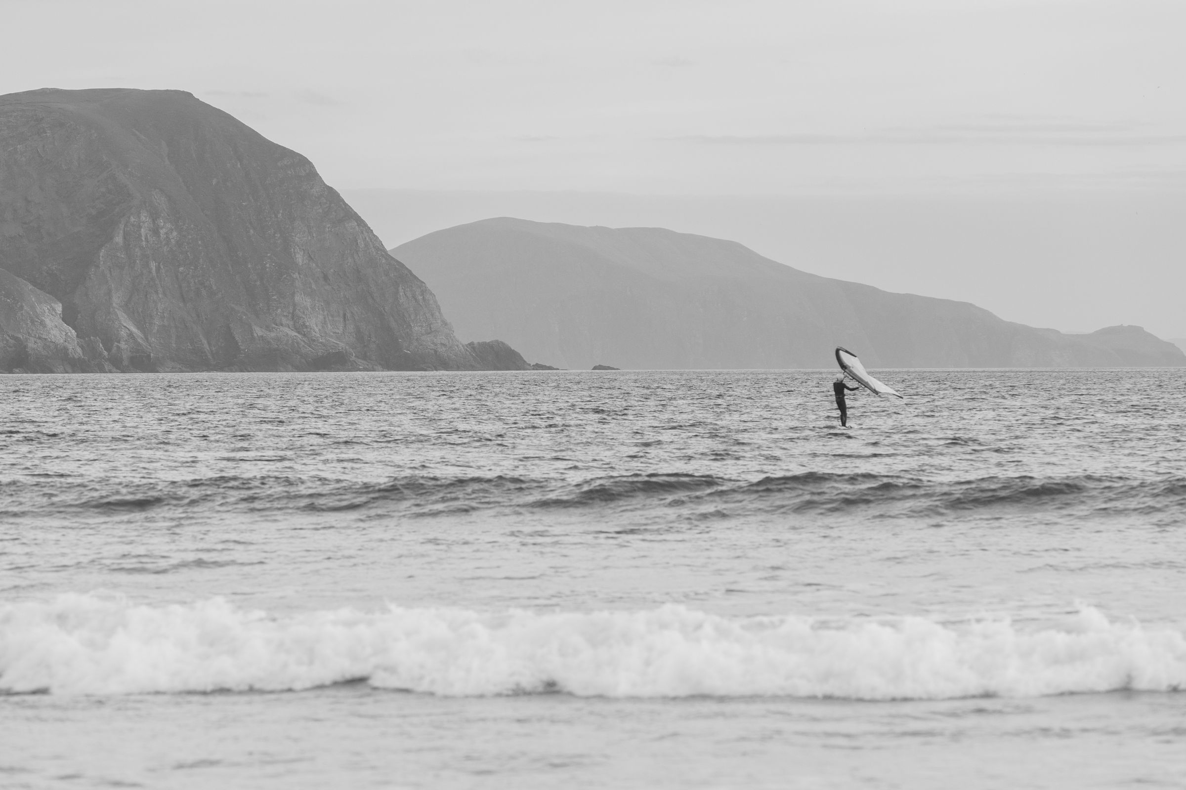 A lone windsurfer navigates the waves in County Mayo, Ireland, under expansive skies