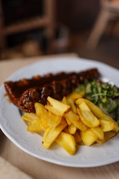 Savory pork ribs with crispy fries and fresh greens on a white plate.