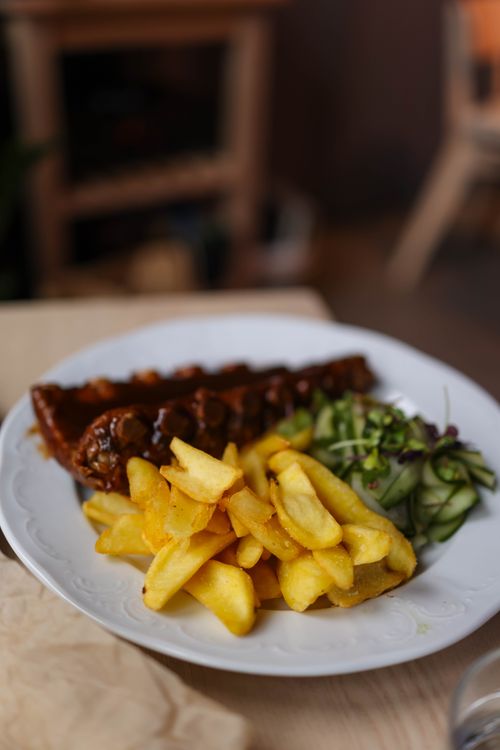 Free Savory ribs with crispy fries and fresh salad on a white plate, perfect for food lovers. Stock Photo