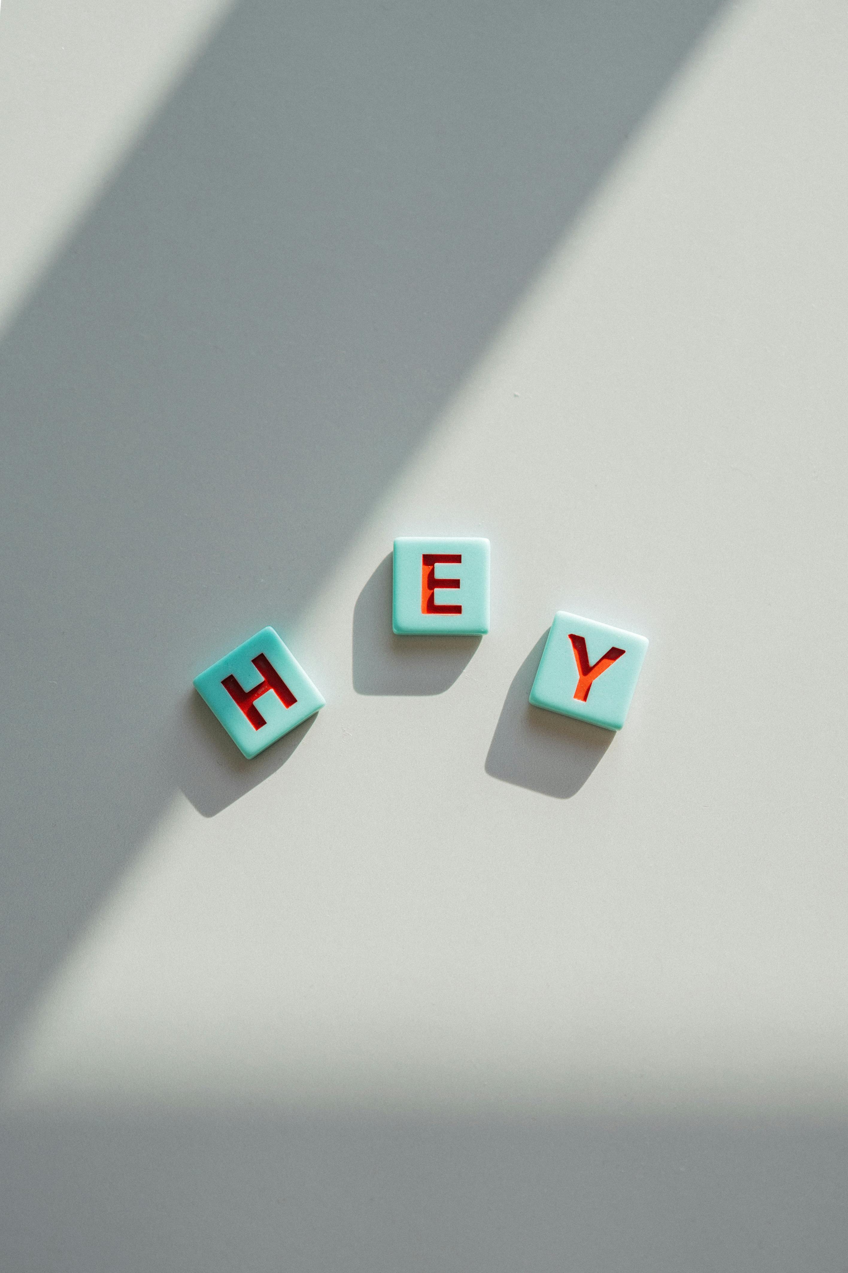 Gratis Gaya minimalis yang cerah dengan tiga ubin Scrabble membentuk kata 'HEY' pada latar belakang terang. Foto Stok