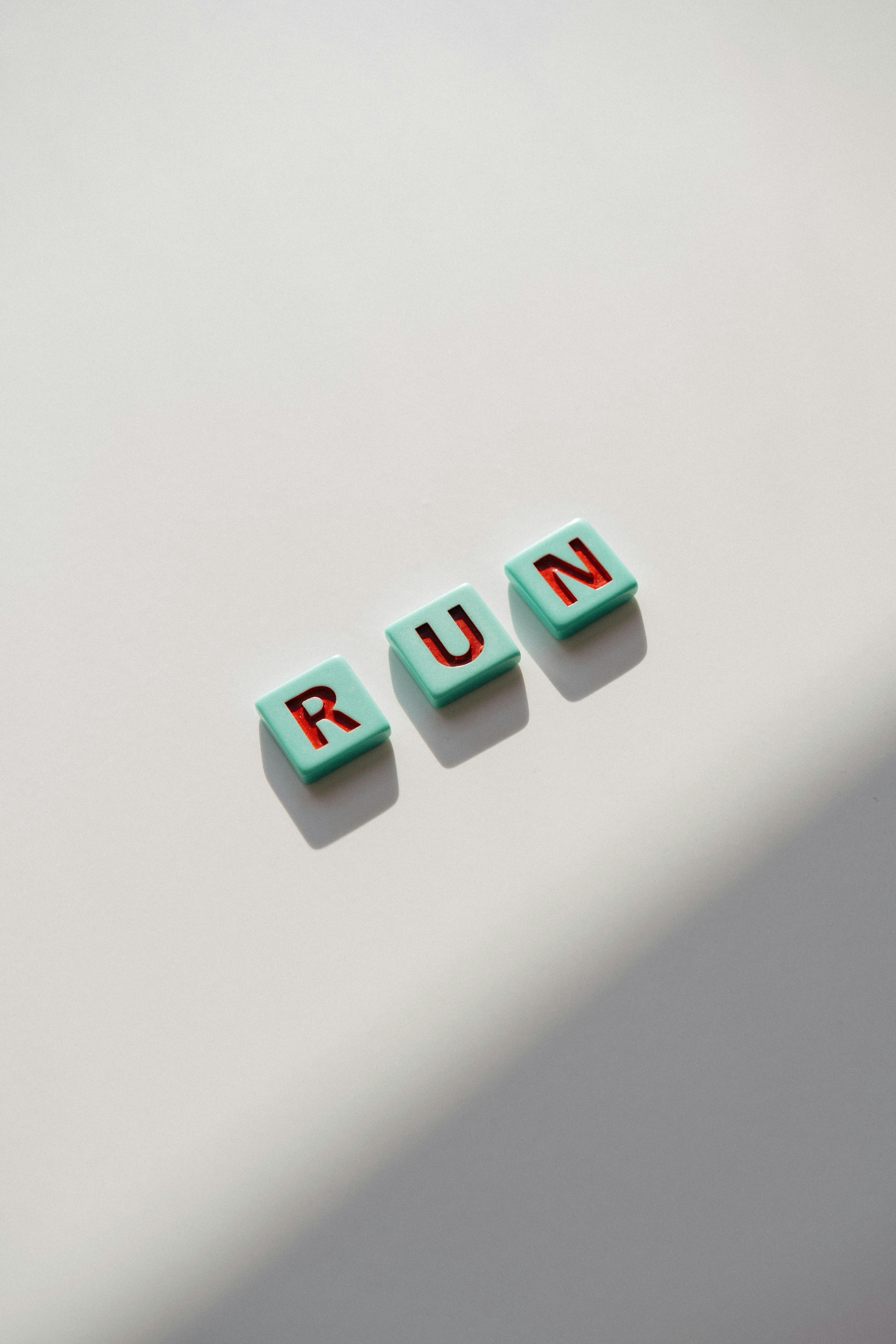 Zadarmo Minimalistické usporiadanie dlaždíc s nápisom „RUN“ na mäkkom slnečnom svetle, ideálne pre motivačné témy. Fotka z fotobanky