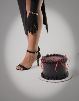 A stylish black cake paired with a woman's high heel and glove for a sophisticated touch.