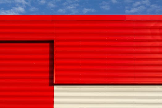 Close-up of a red and cream industrial building facade with geometric lines under a blue sky.