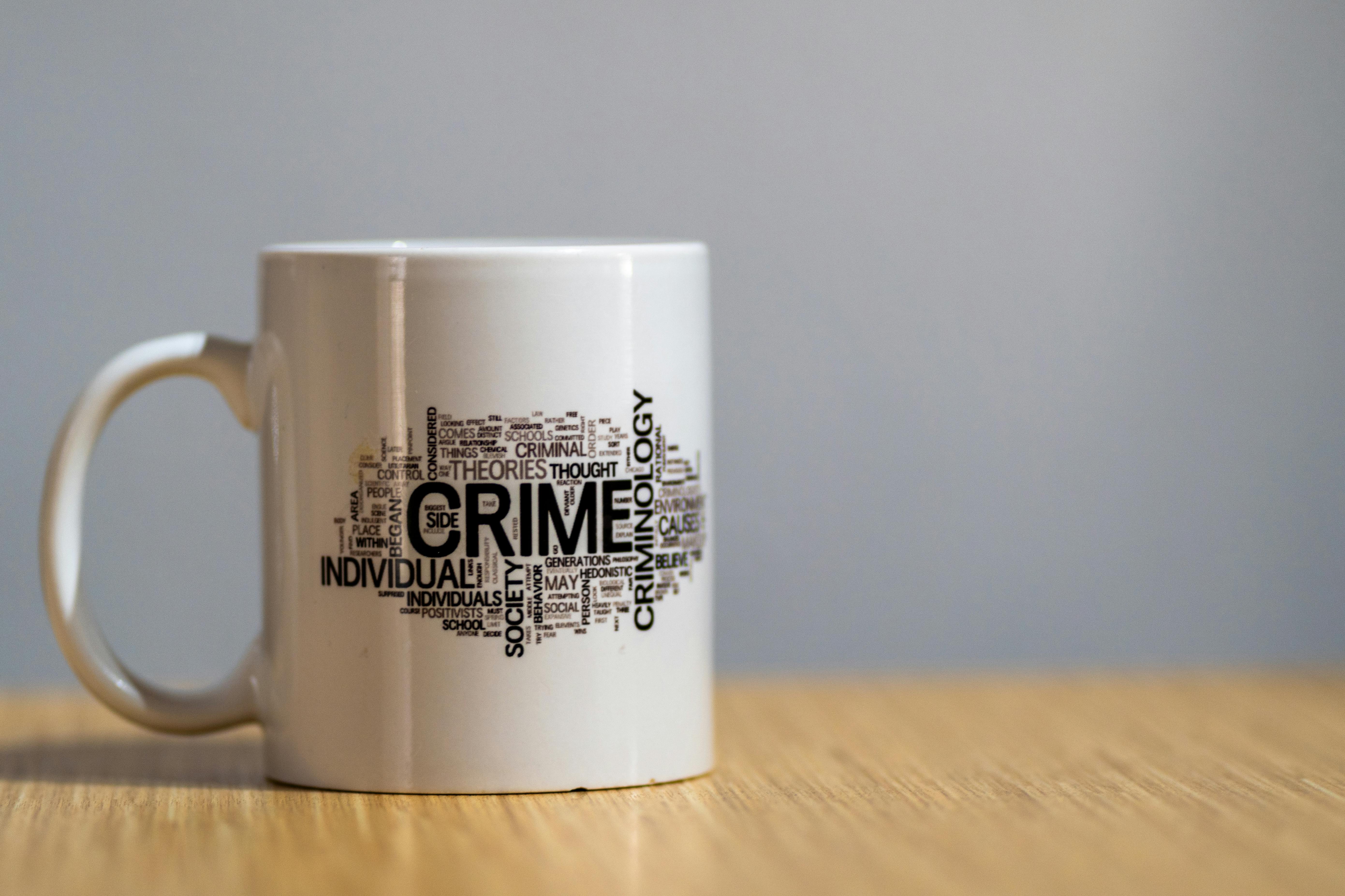 White ceramic mug with criminology-themed word cloud design on wooden surface.