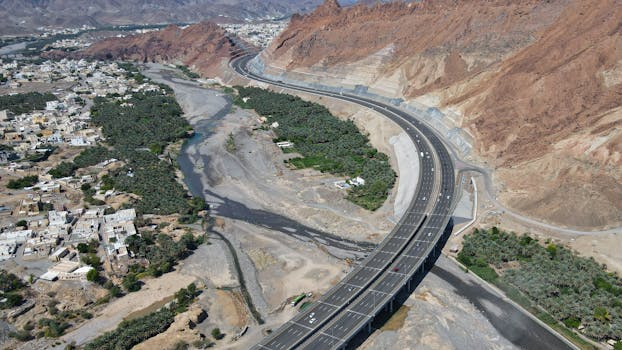 Aerial shot of a highway curving through a mountain valley and rural landscape.