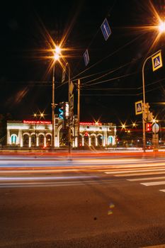 Illuminated urban street at night with vibrant light trails and traffic motion.