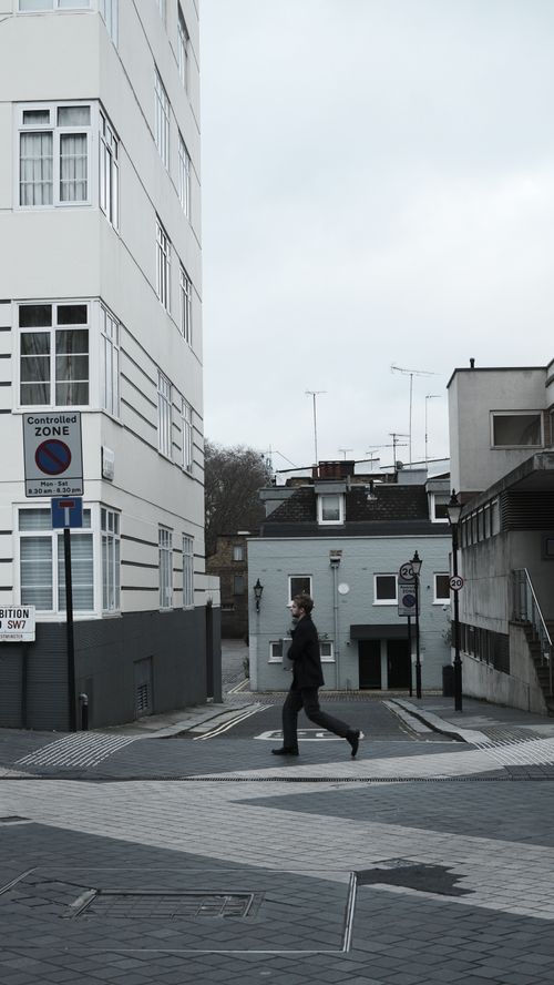 Free A man walks in a city street with modern buildings and overcast sky. Stock Photo