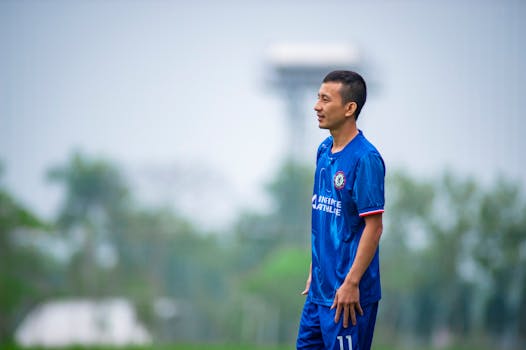 Soccer player in blue uniform on a grassy field in Hà Nội, Việt Nam.