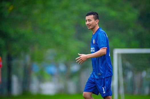 A young man in a blue soccer uniform enjoying an outdoor game during a rainy day in Hanoi, Vietnam.