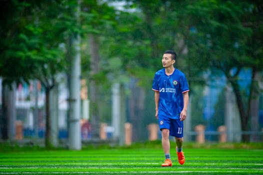 A soccer player in a blue jersey stands on a lush green field in Hanoi.
