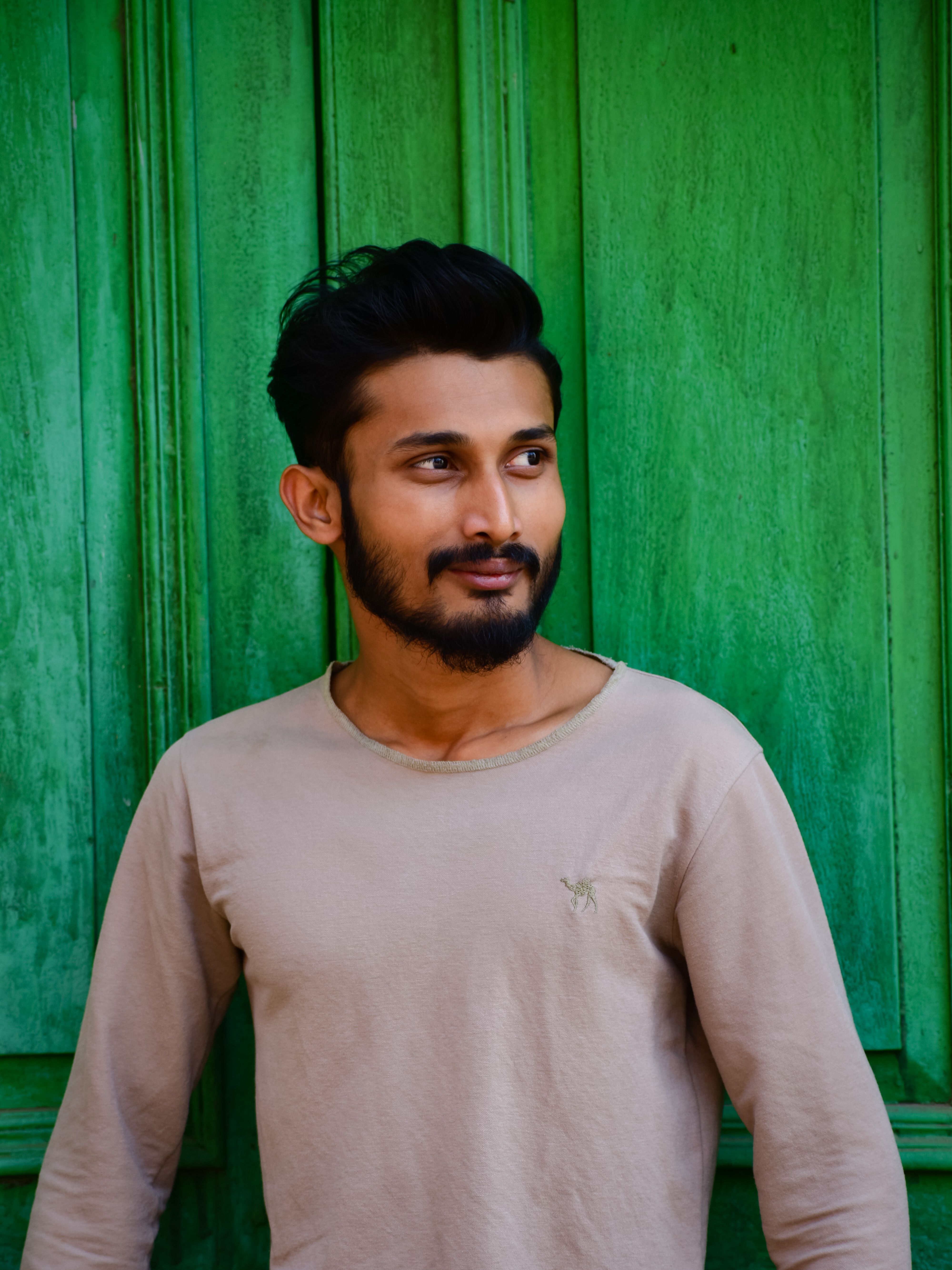 Stylish young man with a beard posing against a vibrant green wooden background.