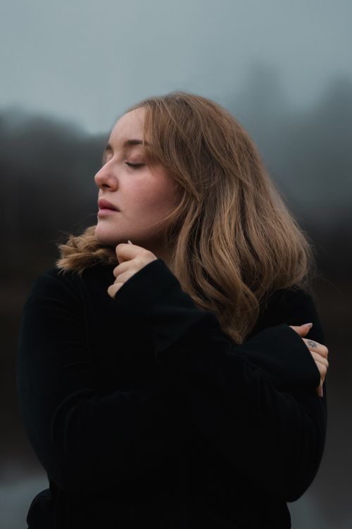 Free Young woman wrapped in black clothing outdoors, conveying moodiness in a misty setting. Stock Photo