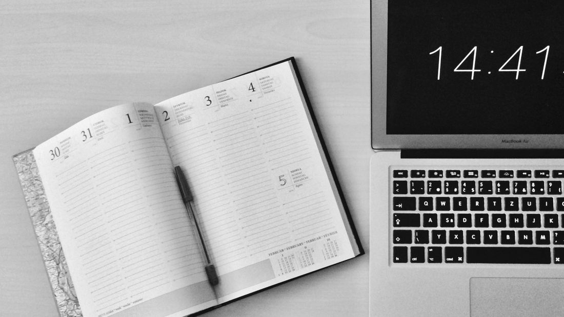 Agenda ouvert et ordinateur portable affichant l’heure sur un bureau