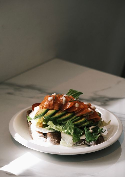 Free Delicious open sandwich with avocado, salmon, and greens on a marble table. Stock Photo