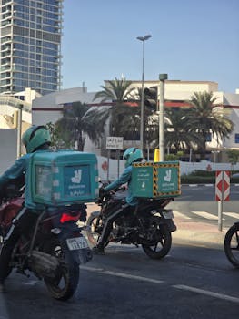 Deliveroo riders navigate Dubai streets with delivery boxes on motorbikes.