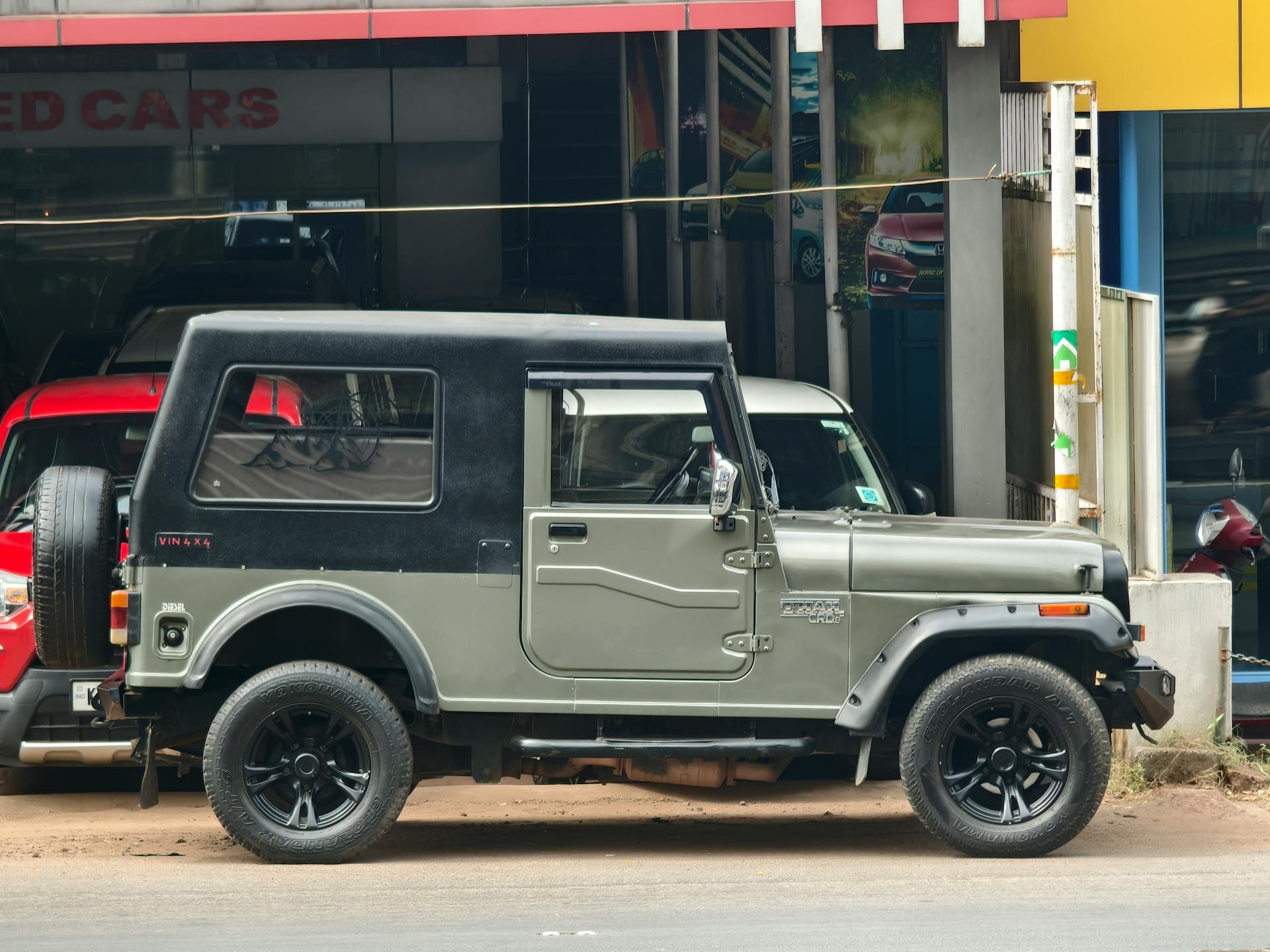 A classic green SUV parked in front of a car dealership.