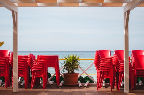 Stacks of red plastic chairs on wooden terrace of cafe on seashore being closed