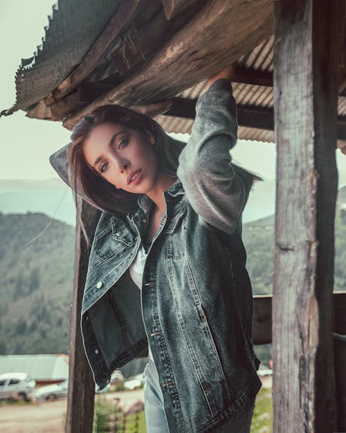 Woman Wearing Blue Denim Jacket Standing While Holding On Wooden Slab