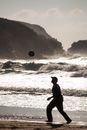 Side view full body of man running after ball on sandy coast along powerful stormy sea with cliffs on background