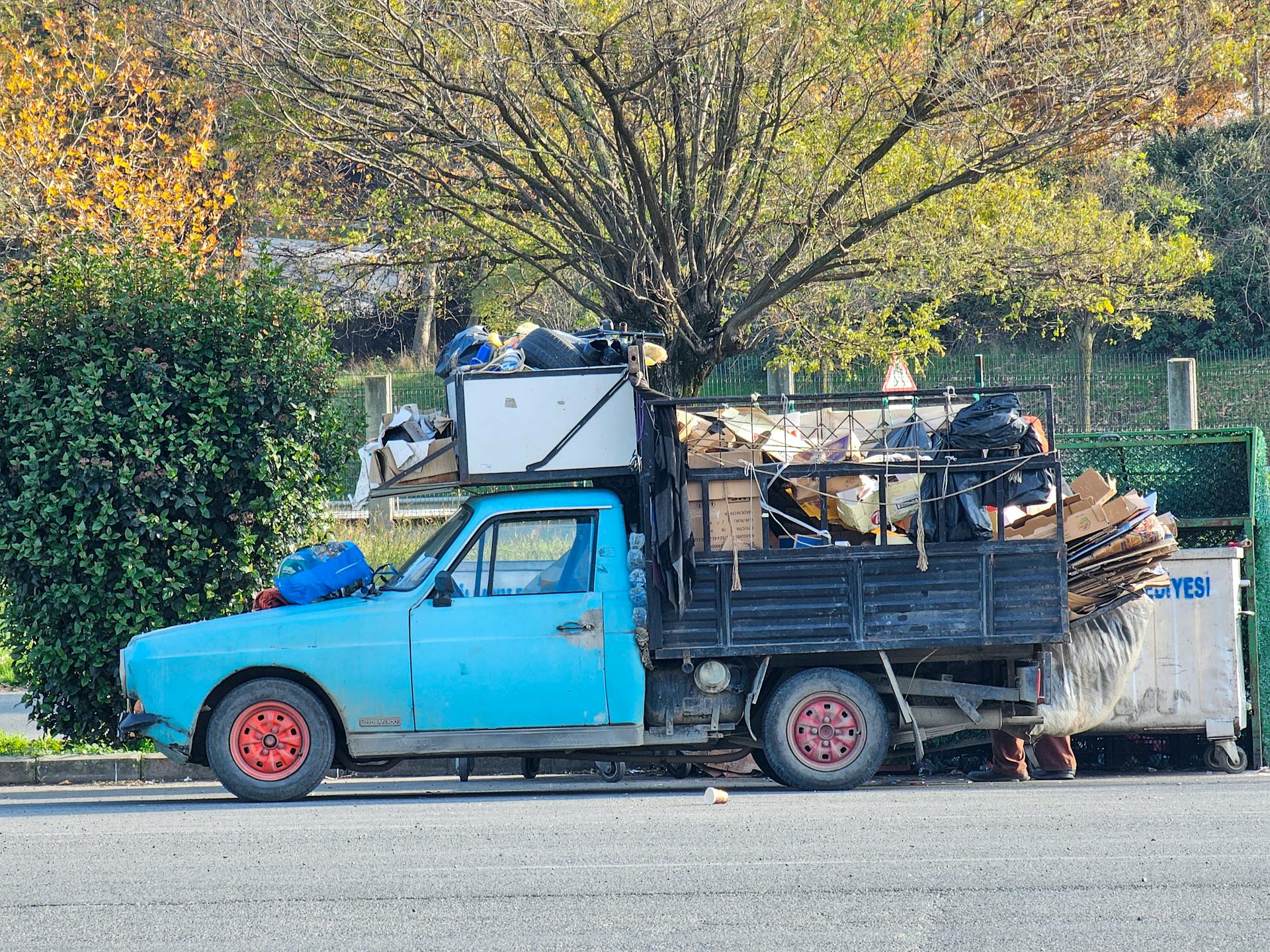 Side view of a vintage blue truck loaded with recyclable waste on a sunny day.