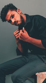 Dynamic portrait of a young man striking a confident pose in a dark outfit against a neutral background.