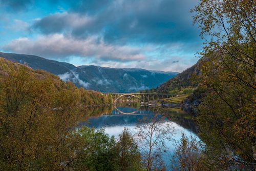 Free Stunning autumn landscape in Norway featuring a reflected bridge on a calm lake with vibrant foliage. Stock Photo