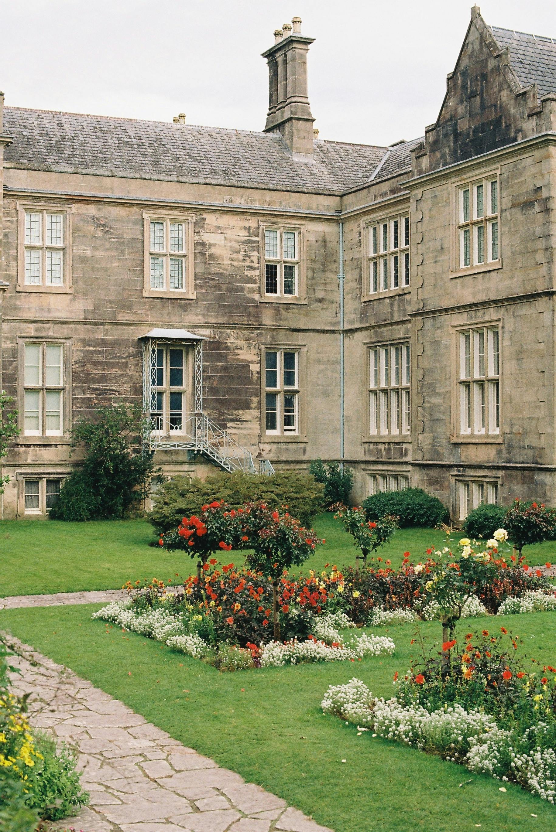 Charming historic stone mansion facade with lush garden and pathway.