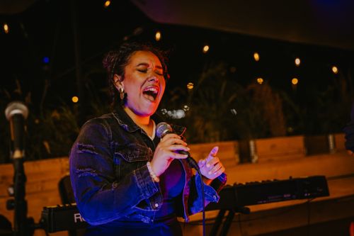 Free Female singer performing live outdoors at night with string lights. Stock Photo