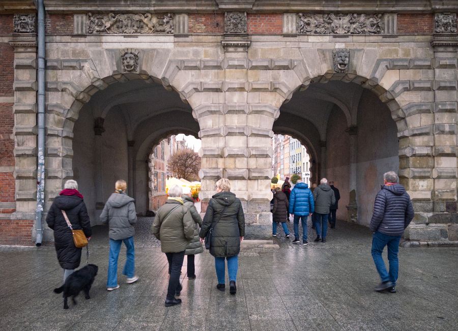 Tourists walk through a historic stone gate in Gdańsk, Poland, during a cool day.