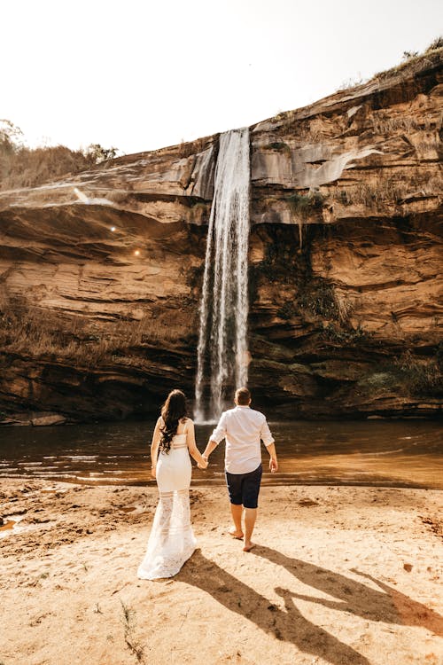 Женщина и мужчина идут через водопад, держась за руки
