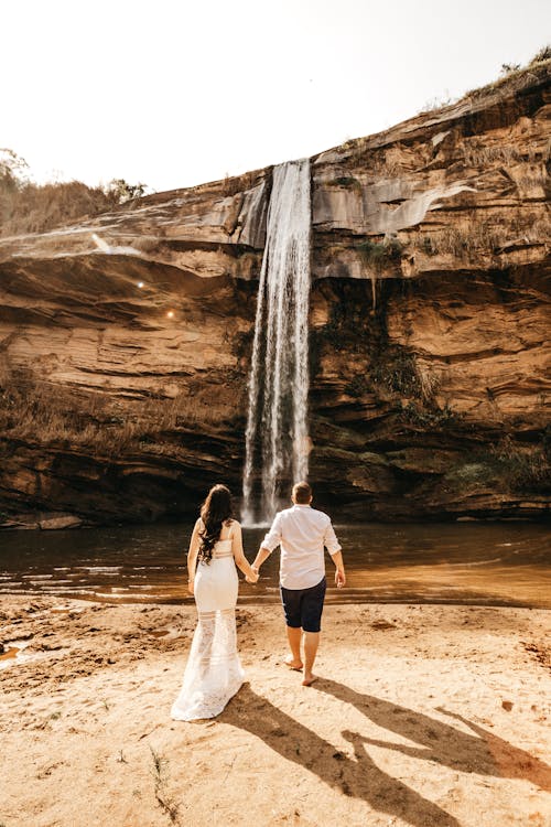 Donna E Uomo Che Cammina Attraverso Le Cascate Tenendo Le Mani