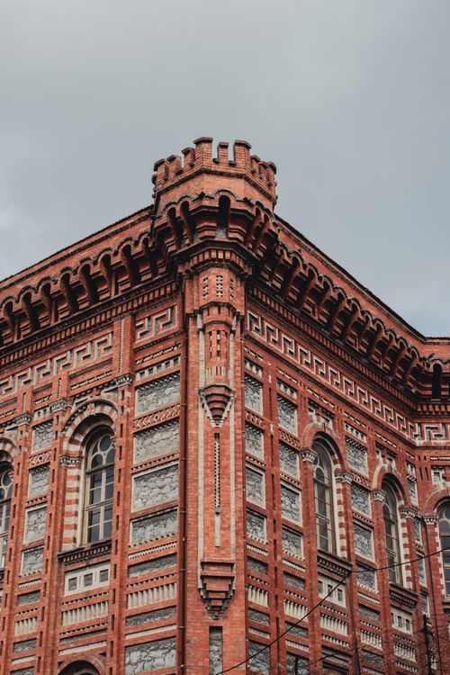 Free A historic red brick building showcasing intricate Gothic architectural details under a cloudy sky. Stock Photo