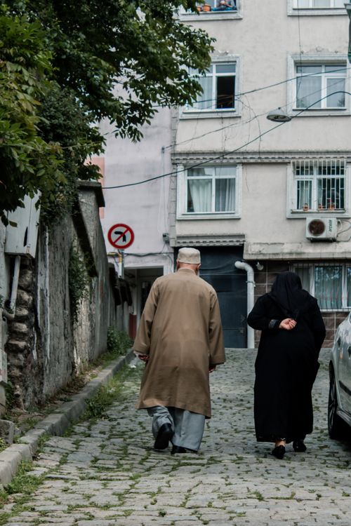 Free Elderly couple walking on cobblestone street in a residential area, showcasing everyday life. Stock Photo
