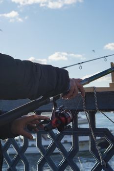 Close-up view of hands holding a fishing rod on a pier with sea in the background.