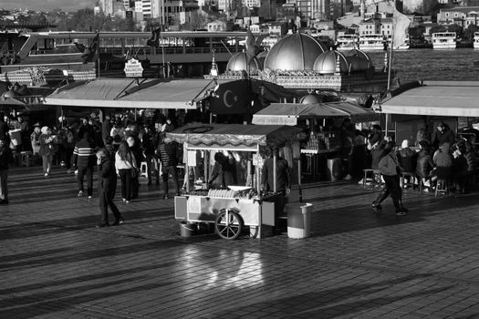 Black and white photo of a vibrant Turkish street market by the waterfront with domed architecture.