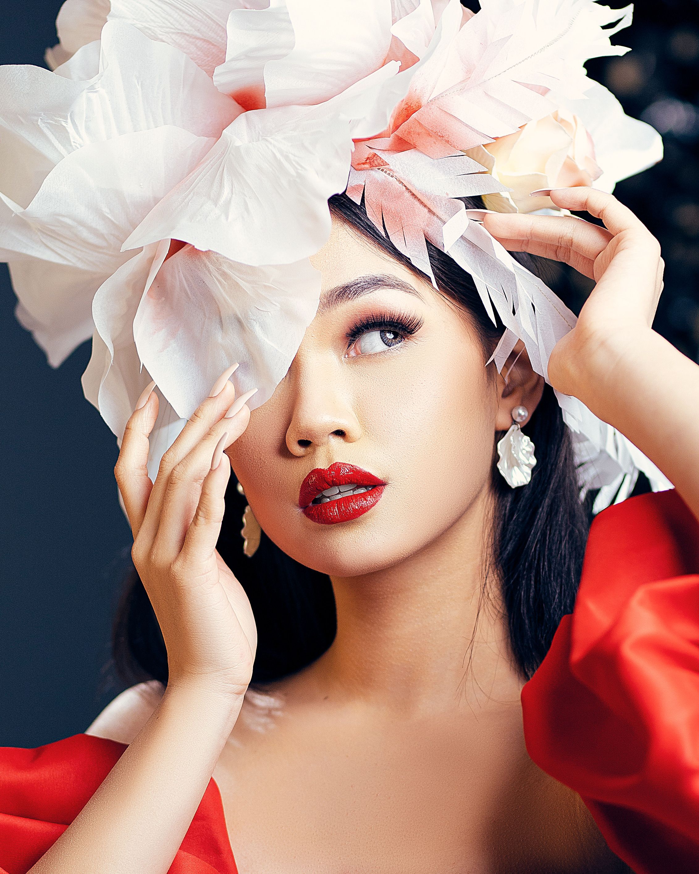 Striking portrait of a woman wearing a large floral headpiece and bold red lipstick.