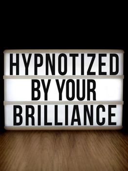 Lightbox with an inspirational message 'Hypnotized by Your Brilliance' on a wooden surface.