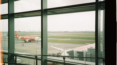 View of an AirAsia plane taxiing on the runway from inside the airport terminal.