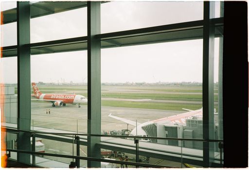 View of an AirAsia plane taxiing on the runway from inside the airport terminal.