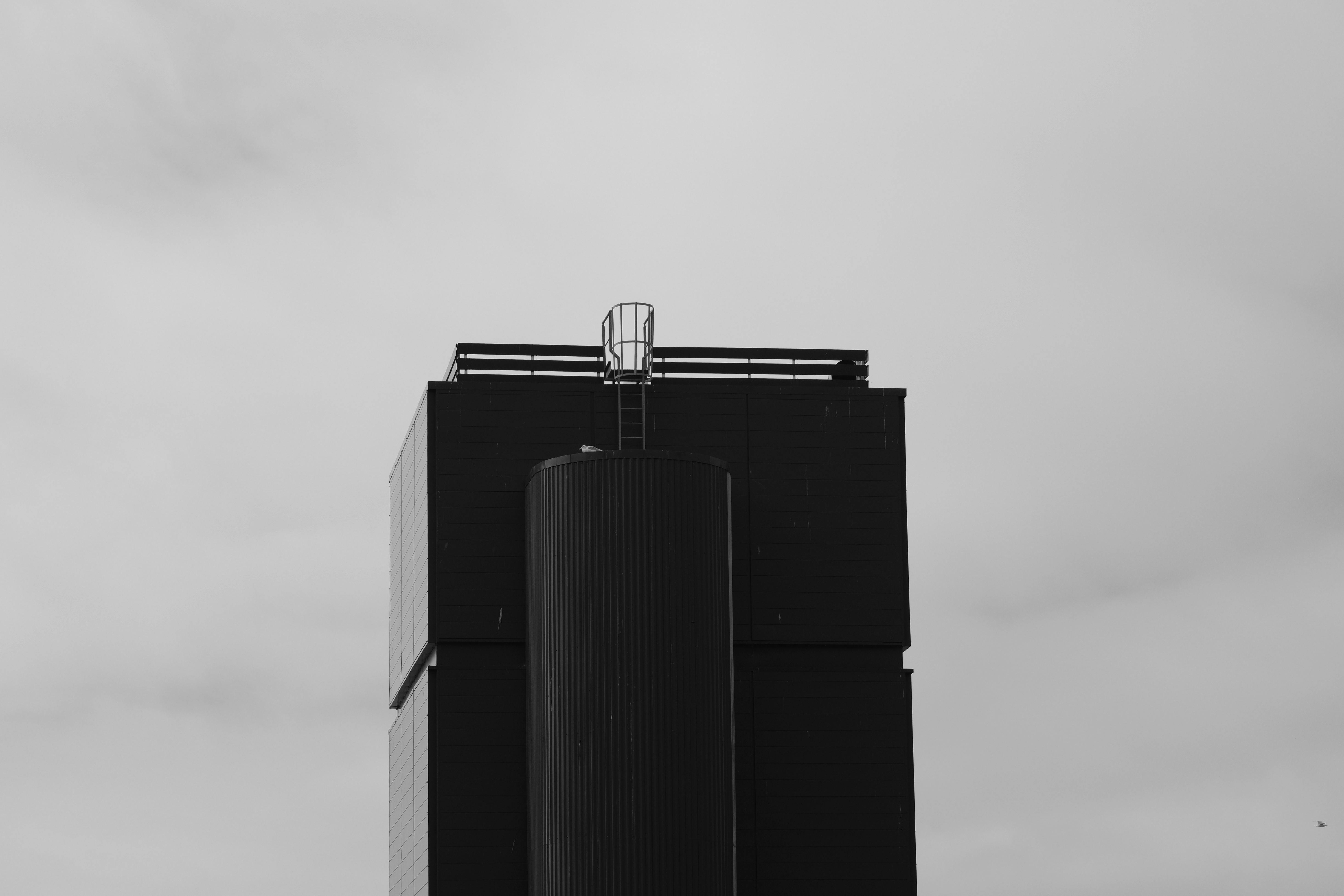 Kostenlos Schwarzweißfoto eines modernen Industriegebäudes unter bewölktem Himmel. Stock-Foto