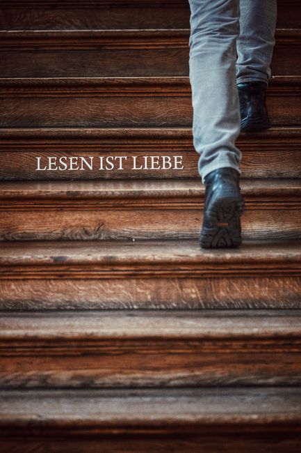 A solitary person ascends a wooden staircase with the text 'LESEN IST LIEBE' in focus.