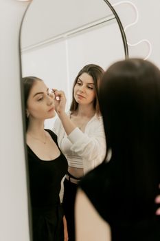Two women engaged in makeup application in front of a mirror.