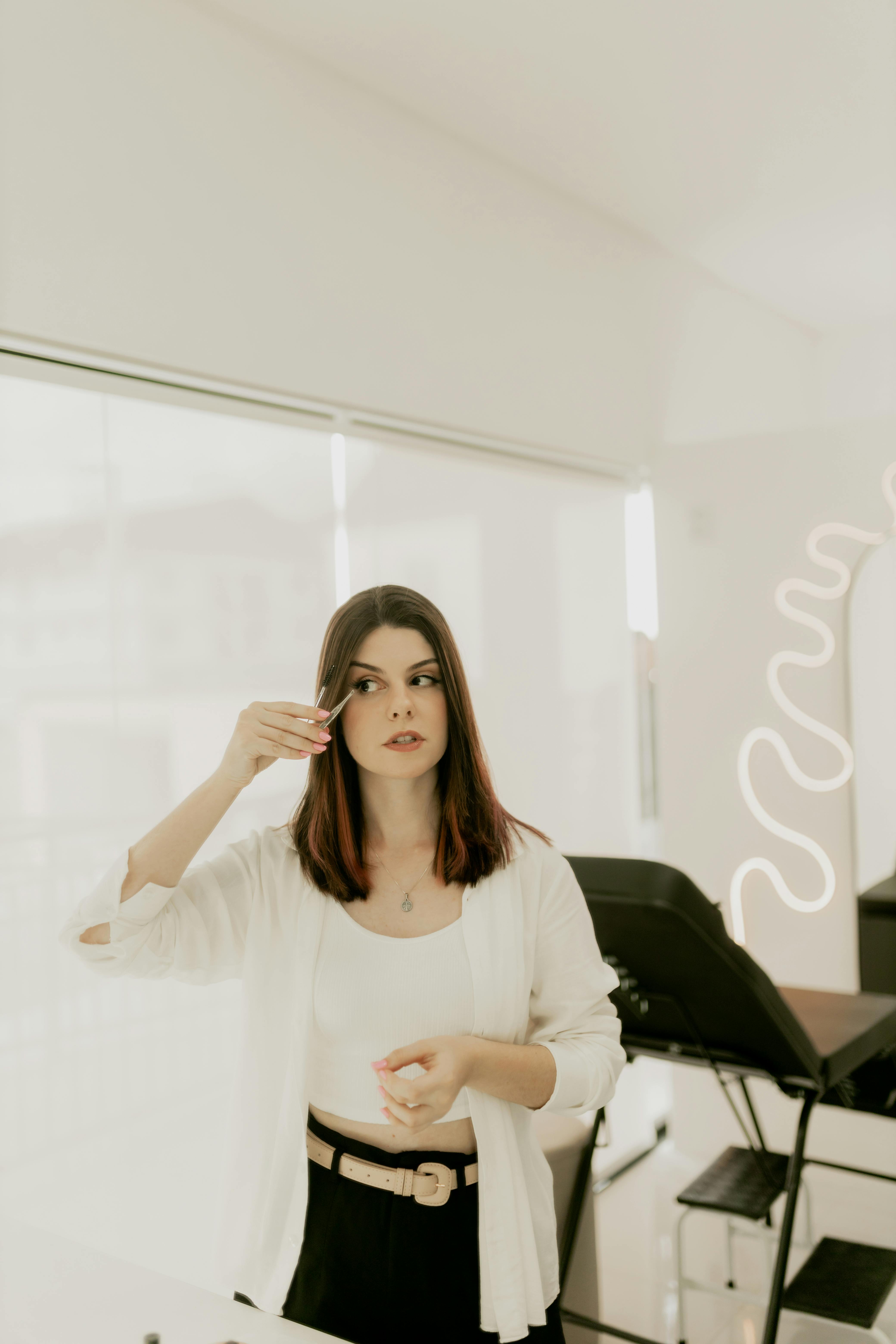 A woman applies makeup in a contemporary room with a soft, neutral tone.