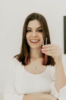 Woman smiling while holding makeup brushes, enjoying beauty routine.