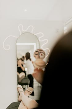 Woman applying makeup in a modern salon with mirror reflection.