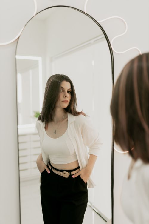 Free Young woman looking at her reflection in a modern, stylish mirror. Stock Photo
