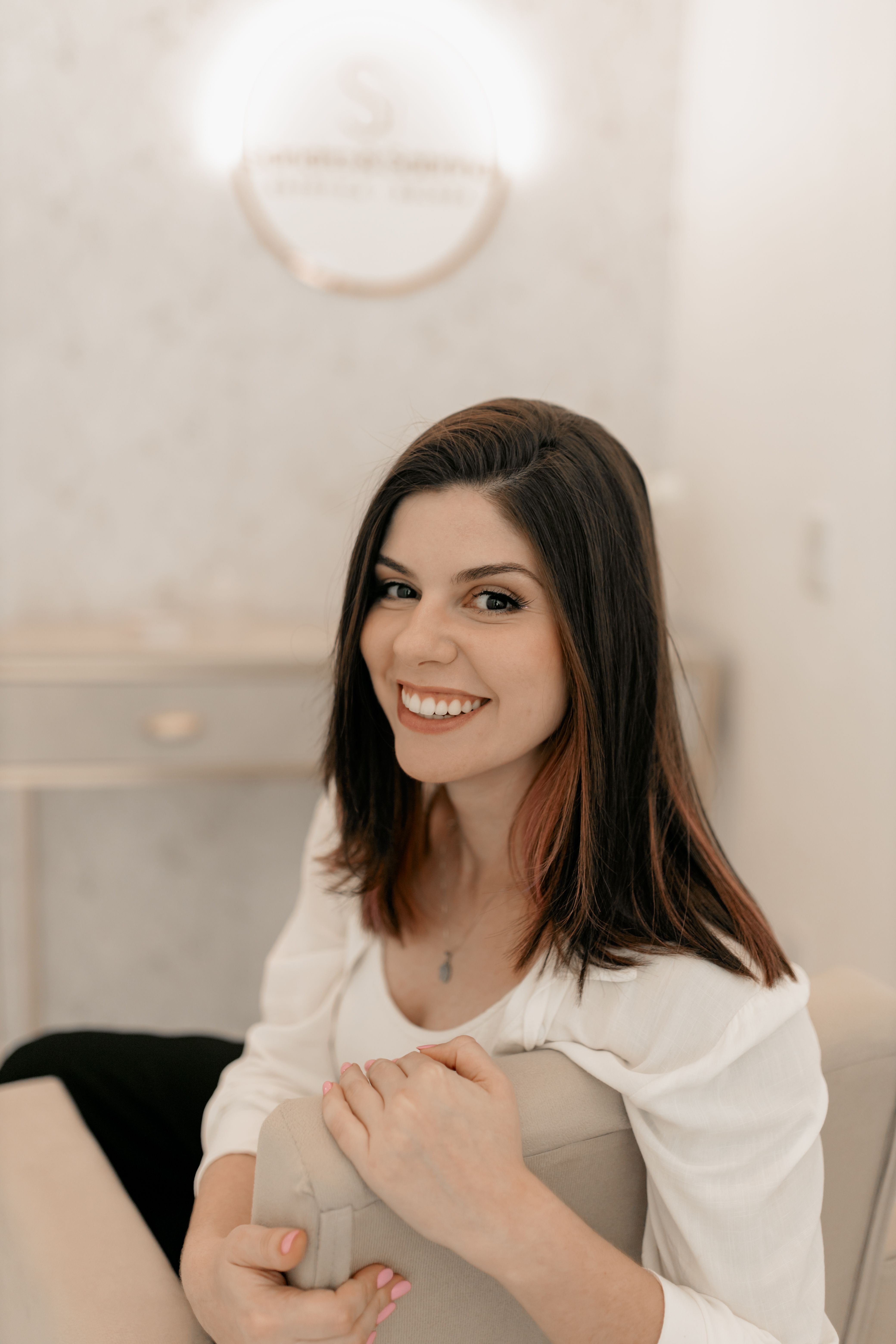 Young woman smiling while seated in a cozy indoor setting.