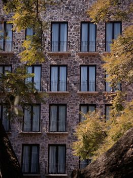 Colonial stone building with multiple windows framed by autumn trees, showcasing elegant architecture.