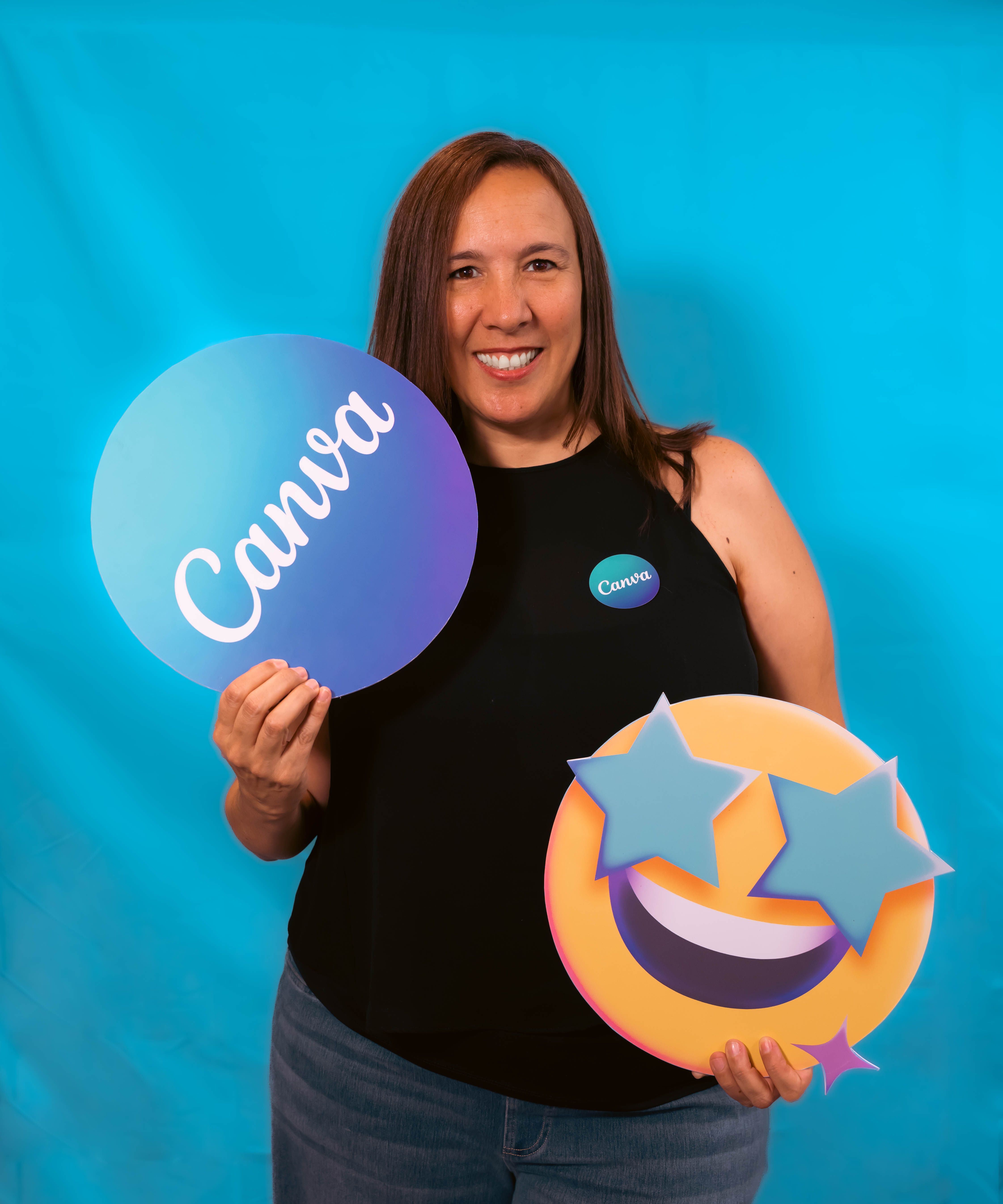 Portrait of a woman smiling, holding Canva and emoji signs against a blue backdrop.