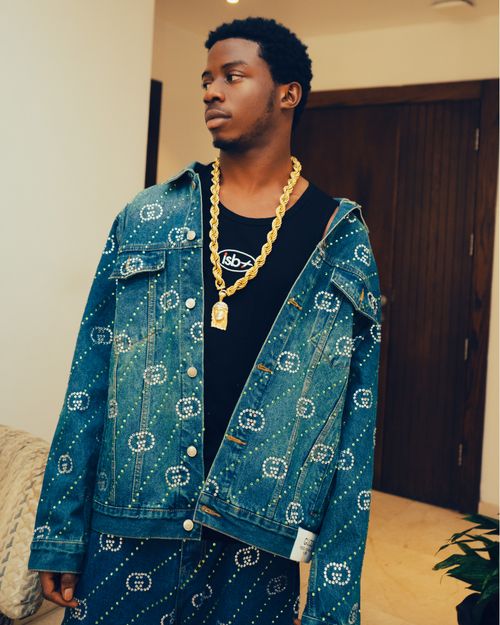 Free Young adult wearing a designer denim jacket and gold chain indoors. Stock Photo